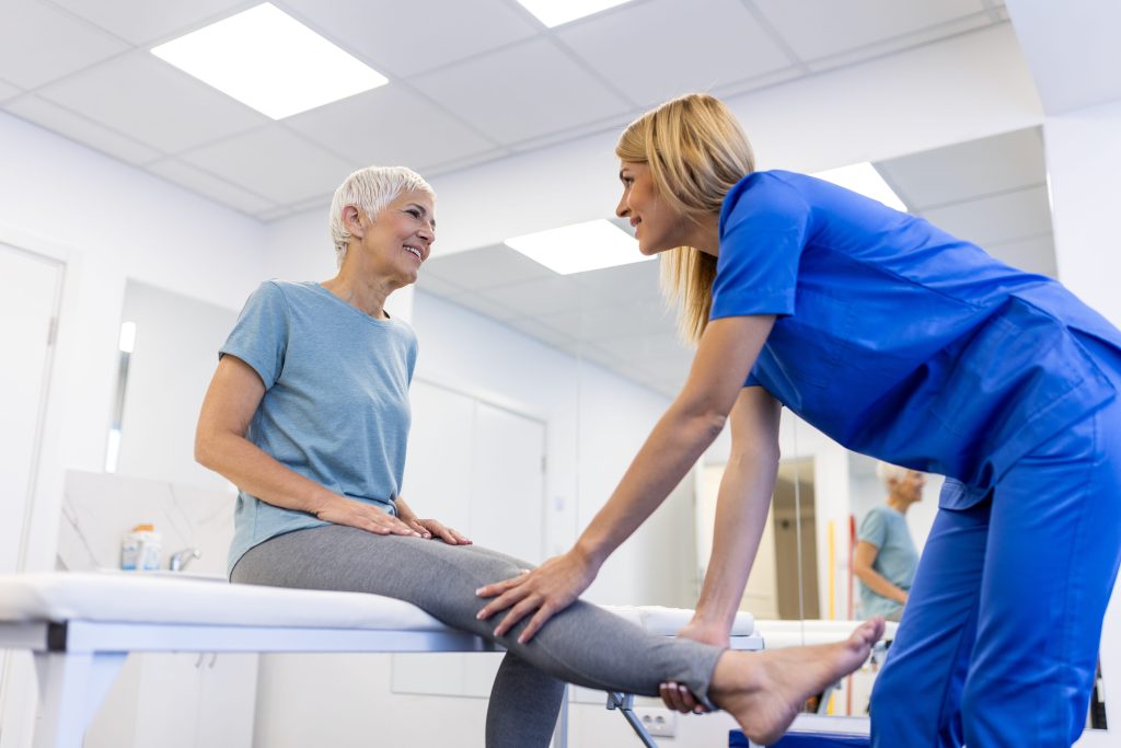 chiropractor helping elderly woman with leg physiotherapy